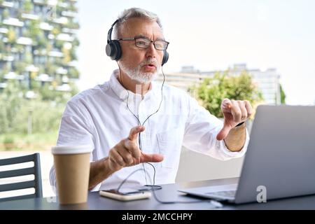 Old senior business man having hybrid remote call meeting on laptop outdoors. Stock Photo