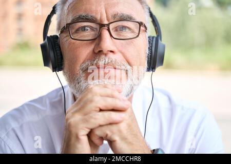 Older senior adult business man wearing headphones looking at camera. Stock Photo