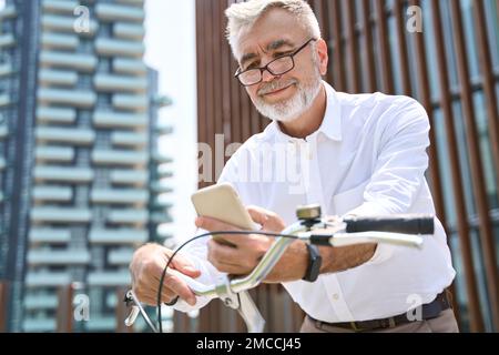 Older active man using mobile phone hiring bike in app to ride in the city. Stock Photo