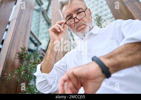 Busy older senior business man looking at wristwatch standing outdoors. Stock Photo