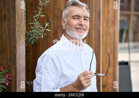 Smiling classy older senior business man looking at camera standing outdoors. Stock Photo