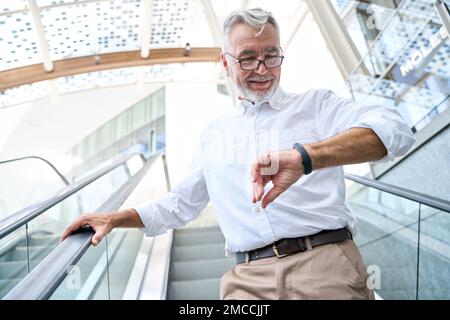 Older senior business man looking at wristwatch or fitness tracker outdoors. Stock Photo
