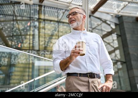 Confident senior older business man standing outdoors holding coffee. Stock Photo