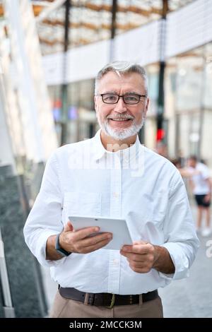 Older senior professional business man using digital tablet standing outdoors. Stock Photo