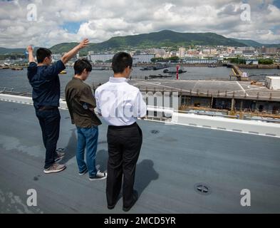 Sho Tagawa, a member of the Yatsushiro Student Volunteer Group (YSVG) on a tour aboard USS America (LHA 6), waves to Sailors aboard the amphibious dock landing ship USS Ashland (LSD 48) as the ship returns to port at Commander, Fleet Activities Sasebo (CFAS) June 29, 2022. The YSVG toured CFAS and met with the U.S. Consulate from Fukuoka as part of an ongoing correspondence between the YSVG and the consulate that began following U.S. military support for Japan Self Defense Force relief efforts for the 2016 Kumamoto earthquakes. Stock Photo