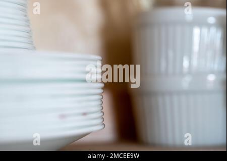 Narrow depth of field picture of an open kitchen cabinet stacked ceramic plates and bowls. Stock Photo