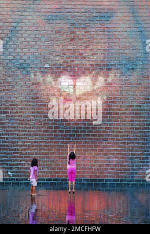 Two young girls wait for the Crown Fountain, an art display showing video images of various city people, to gush water in Millennium Park, Chicago Stock Photo