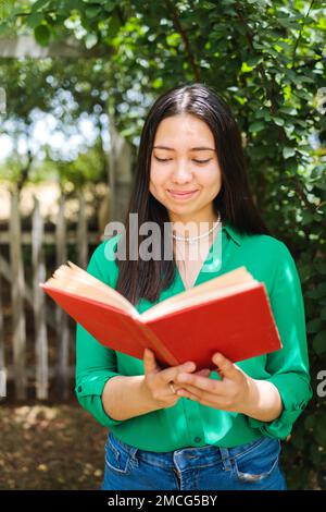 Beautiful smiling young farmer woman reading book in the field. Vertical shot. World book day Stock Photo