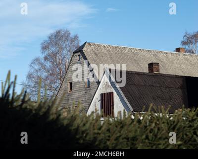 Old house with asbestos sheets on the exterior wall and on the roof. The weathered cement plates with fibres are forbidden in Germany. Stock Photo