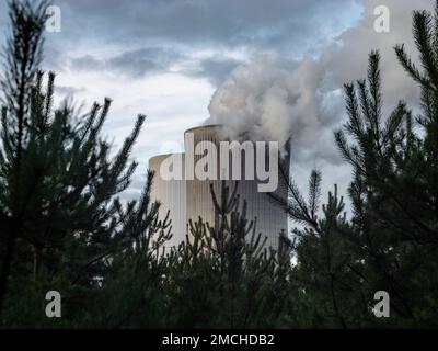 Air pollution emitted by a lignite fired power station in the green nature. Big concrete chimney with smoke. Dark moody footage of the energy industry Stock Photo