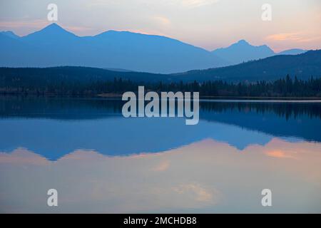 Calm water on Pyramid Lake at dusk reflecting mountain silhouettes in Jasper National Park, Alberta, Canada Stock Photo