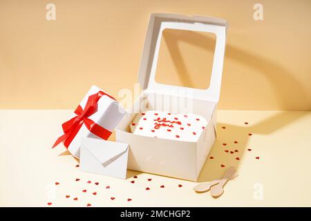 Opened box with tasty bento cake, gift and envelope on beige table. Valentine's Day celebration Stock Photo