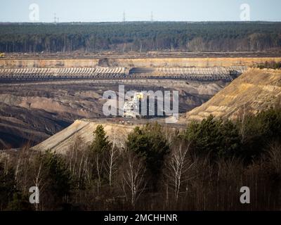 Machinery in front of a brown coal open pit landscape. Human made hole in the nature to exploit natural resources like lignite. Mining fossil fuels. Stock Photo