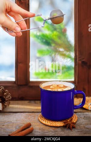 cinnamon powder from sieve flying on hot cocoa with marshmallows in ceramic cup on wooden table Stock Photo