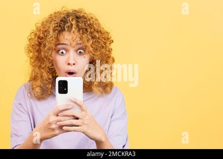 Surprised woman with curly hair using the mobile phone Stock Photo