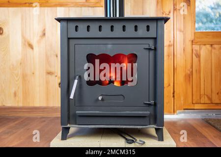 Rustic cast iron stove with the fire lit inside to heat the house. Stock Photo