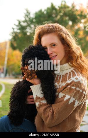 Young woman hugging her black puppy poodle dog in a park. Stock Photo