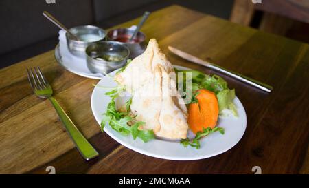 Samosa is a fried or baked dumpling with savory filling, such as seasoned potatoes, onions, peas, meat, or lentils. Traditional Indian Food. Stock Photo