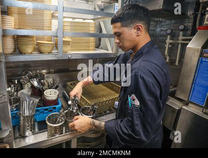 PHILIPPINE SEA (July 6, 2022) Gas Turbine Systems Technician (Electrical) Fireman Zion Mendoza, from Jacksonville, Florida, cleans cutlery in the scullery aboard Arleigh Burke-class guided-missile destroyer USS Benfold (DDG 65). Benfold is assigned to Commander, Task Force (CTF) 71/Destroyer Squadron (DESRON) 15, the Navy’s largest forward-deployed DESRON and the U.S. 7th Fleet’s principal surface force. Stock Photo