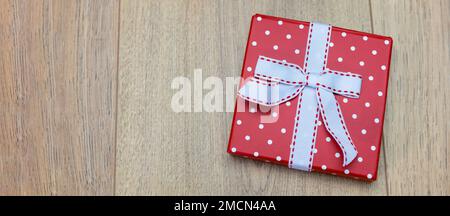 red white polka dot gift box with white ribbon on wooden background, bannerr Stock Photo