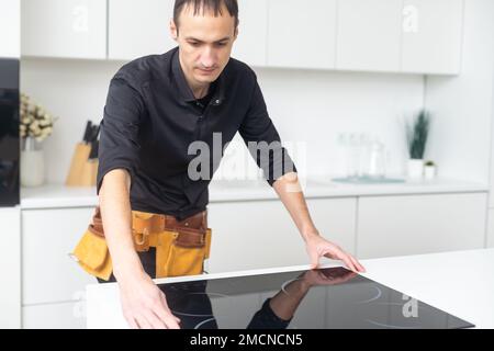 Man electrical repairs kitchen surface apartment. Installing hob in countertop. Man bought new kitchen furniture and appliances. Process installing an Stock Photo