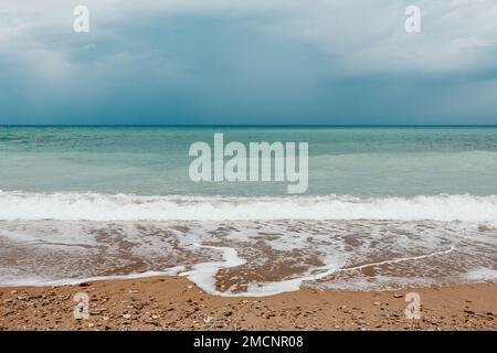 Overcast sky on rainy day with foamy waves rolling towards golden sand beach under low warm sun light. Nobody. Holiday recreation concept. Abstract Stock Photo