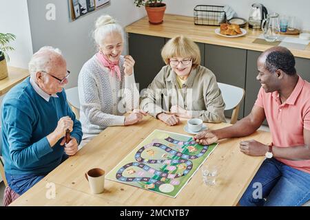 High angle view of senior friends laughing and smiling while playing board game at table in the kitchen Stock Photo