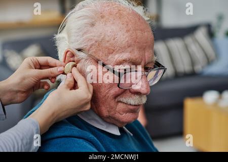 Close-up of caregiver wearing hearing aid into the ear of senior man who having hearing problems Stock Photo