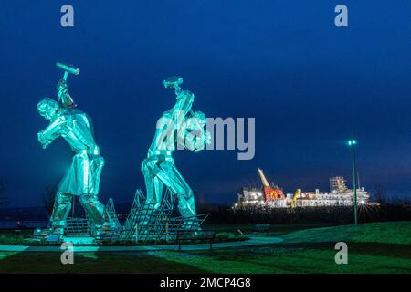 Greenock, United Kingdom. 21 January, 2023 Pictured: The Shipbuilders of Port Glasgow sculpture by John McKenna is illuminated in front of the Glen Sannox Ferry being built at the Ferguson Shipyard. Credit: Rich Dyson/Alamy Live News Stock Photo