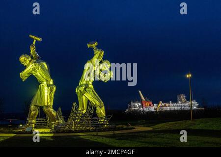 Greenock, United Kingdom. 21 January, 2023 Pictured: The Shipbuilders of Port Glasgow sculpture by John McKenna is illuminated in front of the Glen Sannox Ferry being built at the Ferguson Shipyard. Credit: Rich Dyson/Alamy Live News Stock Photo