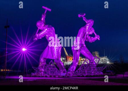 Greenock, United Kingdom. 21 January, 2023 Pictured: The Shipbuilders of Port Glasgow sculpture by John McKenna is illuminated in front of the Glen Sannox Ferry being built at the Ferguson Shipyard. Credit: Rich Dyson/Alamy Live News Stock Photo