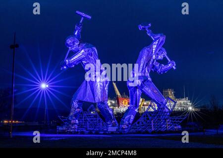 Greenock, United Kingdom. 21 January, 2023 Pictured: The Shipbuilders of Port Glasgow sculpture by John McKenna is illuminated in front of the Glen Sannox Ferry being built at the Ferguson Shipyard. Credit: Rich Dyson/Alamy Live News Stock Photo