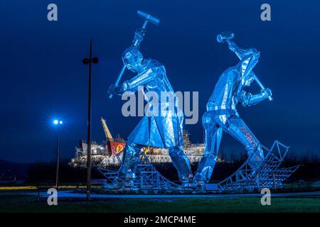 Greenock, United Kingdom. 21 January, 2023 Pictured: The Shipbuilders of Port Glasgow sculpture by John McKenna is illuminated in front of the Glen Sannox Ferry being built at the Ferguson Shipyard. Credit: Rich Dyson/Alamy Live News Stock Photo