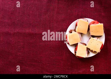 Open sandwich with rye bread, tomatoes, ham and cheese on white plate. Breakfast or brunch concept. Top view, copy space Stock Photo