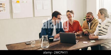 Smiling businesspeople having a discussion using a laptop in a creative office. Group of happy businesspeople sharing ideas while working together on Stock Photo