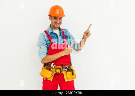 Cheerful male contractor wearing helmet isolated on white background pointing aside while looking at camera Stock Photo