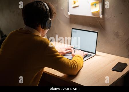 Young man working on laptop in home office. Male student studying in university dormitory at night, typing on laptop computer. Copy space Stock Photo