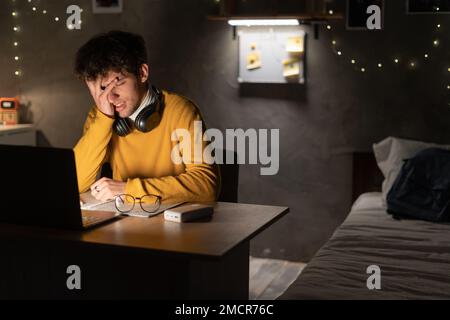Worried and sad student male searching information in a laptop online in a desk at home or dormitory room. Copy space Stock Photo