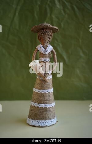 Decorative figure made of straw in the form of woman with flowers. Girl doll in hat with flowers made of handmade threads. DIY. Souvenir toy on green Stock Photo