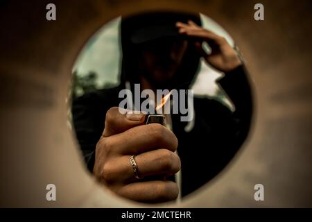 A mysterious man holding a flaming gas lighter in his hand with a ring seen from a tube Stock Photo