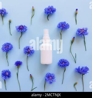 White plastic spray bottle mockup and blue flowers on blue background. Natural organic spa cosmetics and liquid antimicrobial spray concept. Square fl Stock Photo