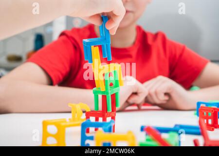 Cropped photo of preteen children sitting at white table, playing board game stacking chairs, putting colorful plastic small chairs in stack for build Stock Photo