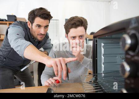 male technician repairing oven with his apprentice Stock Photo