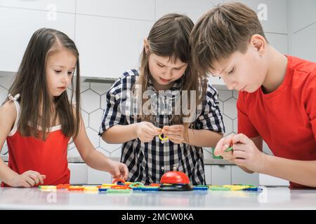 Portrait of group of focused friends children standing at table in kitchen at home, playing board game ring near bell, joining buckling various colorf Stock Photo