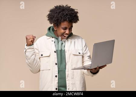Happy excited African teen winner student guy using laptop celebrating win. Stock Photo