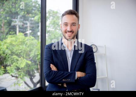 Young caucasian businessman or ceo with leadership smiling in proud in startup business at office, business man or entrepreneur standing and arms cros Stock Photo