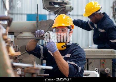 Young caucasian engineer man examining and measuring steel with expertise at lathe factory, worker or technician check and maintenance metal with prof Stock Photo