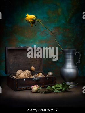 Theme of life and death, still life with nuts in old wooden box next to withered rose in silver jug, studio shot, symbol photo Stock Photo