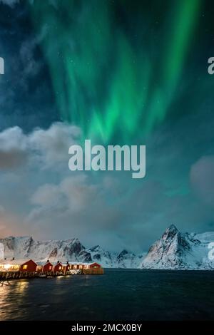 Northern lights over Hamnoy rorbu cabins, snowy mountains behind, Hamnoy, Moskenesoya, Lofoten, Norway Stock Photo
