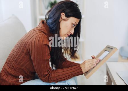 Woman looking sadly at the picture frames in her hands, crying over memories, state of depression and loss of a person Stock Photo